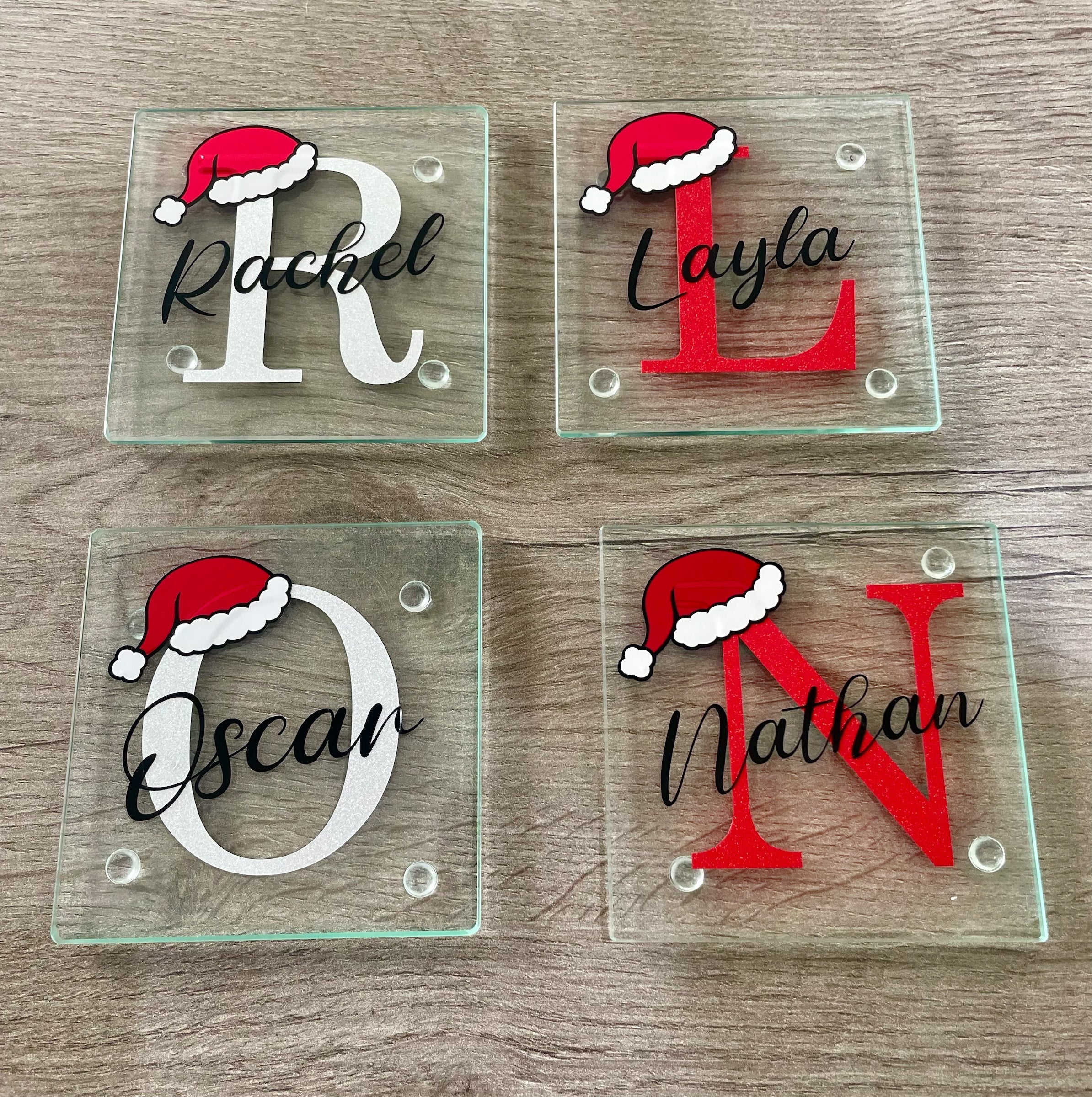 Personalised glass Christmas coasters featuring initials with Santa hats and names in script font, available in red glitter and silver glitter designs.